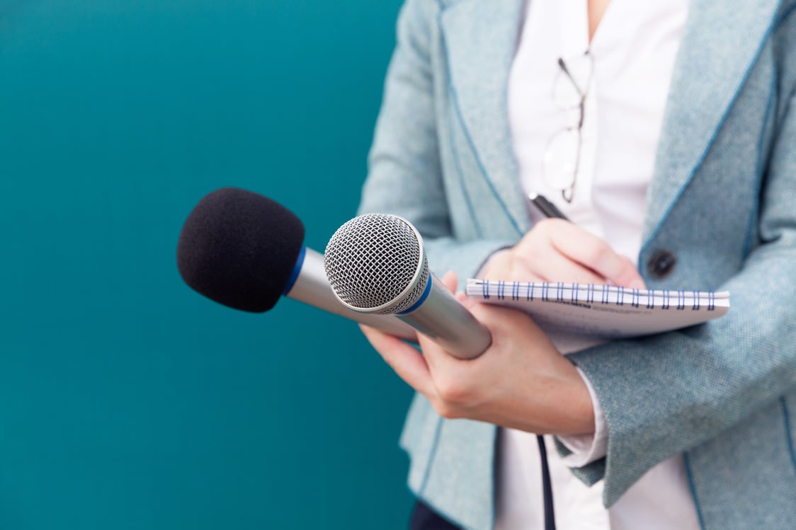 News reporter or TV journalist at press conference, holding microphone and writing notes